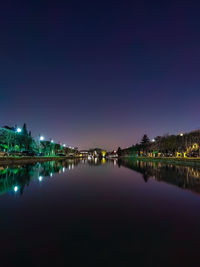 Illuminated buildings by river against sky at night