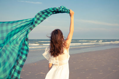 Rear view of woman standing at beach against sky