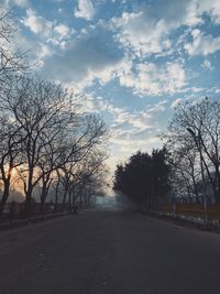 Road amidst bare trees against sky in city