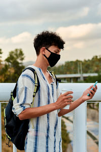 Young afro man with mask is using his mobile on the street