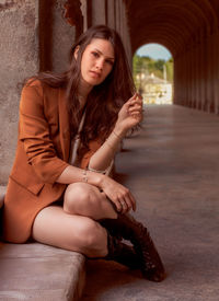 Portrait of young woman sitting against wall