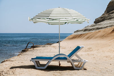 Deck chairs under parasol at beach against clear sky