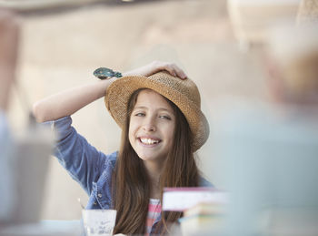 Portrait of smiling teenage girl wearing hat at sidewalk cafe
