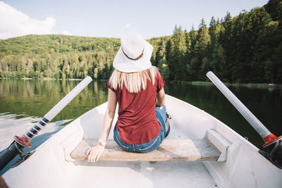 Rear view of woman sitting on boat in lake against sky