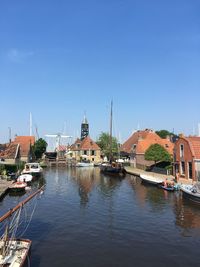 Sailboats moored on river by buildings against clear blue sky