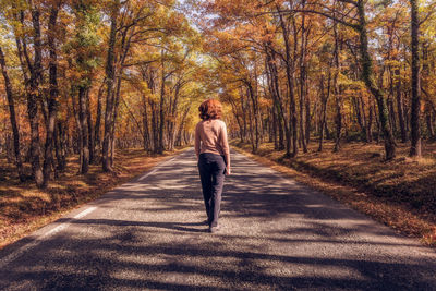 Rear view full length of woman standing on road amidst autumn trees