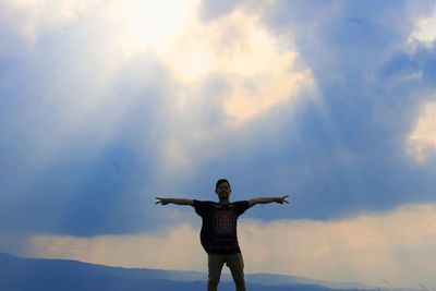 Man with arms outstretched standing against sky