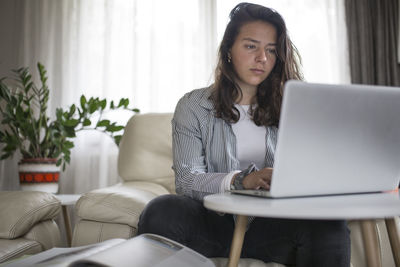 Young woman using phone while sitting on sofa at home