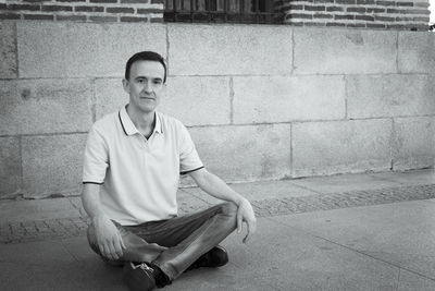 Portrait of young man sitting against wall