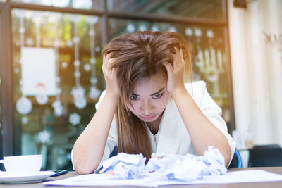 Tensed woman with crumpled papers sitting at cafe