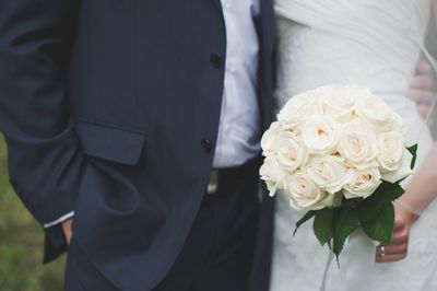 Midsection of bride with bridegroom holding rose bouquet