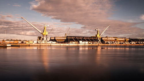 Cranes at harbor against sky