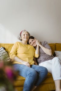 Portrait of smiling woman sitting with elderly mother-in-law on sofa at home