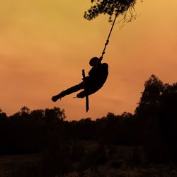 Silhouette man playing swing at sunset