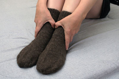 A young woman with slender legs sits on a bed at home in brown woolen socks. 