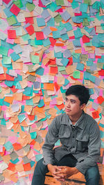 Young man looking away while sitting against wall