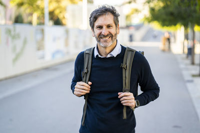 Portrait of smiling mature man wearing a backpack in the city