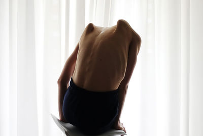 Rear view of shirtless woman looking at window