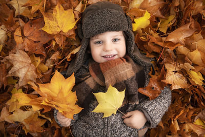 Portrait of smiling boy lying on dry leaves during autumn