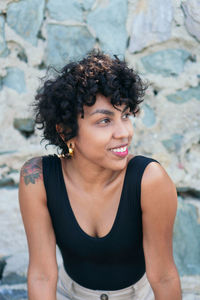 Crop happy young african american female with curly hair and tattoo on shoulder looking away on blurred background