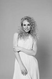 Portrait of woman with curly hair standing against gray background