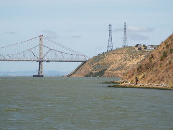 Suspension bridge over river against sky