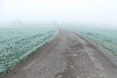 Road amidst field against sky during foggy weather