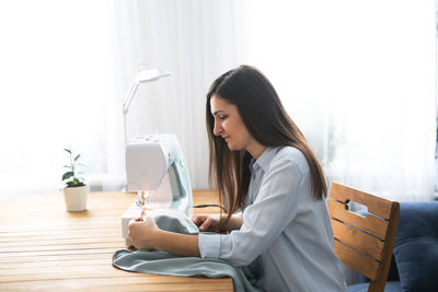 Charming girl with long black hair sews on a sewing machine, concept handmade and mother