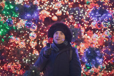 Portrait of man holding caramelized apple during christmas at night