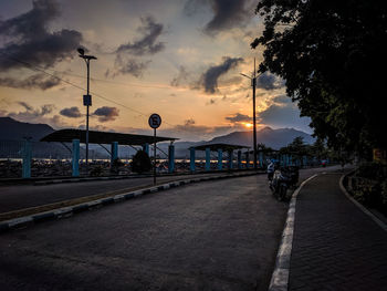 Street lights on road against sky at sunset