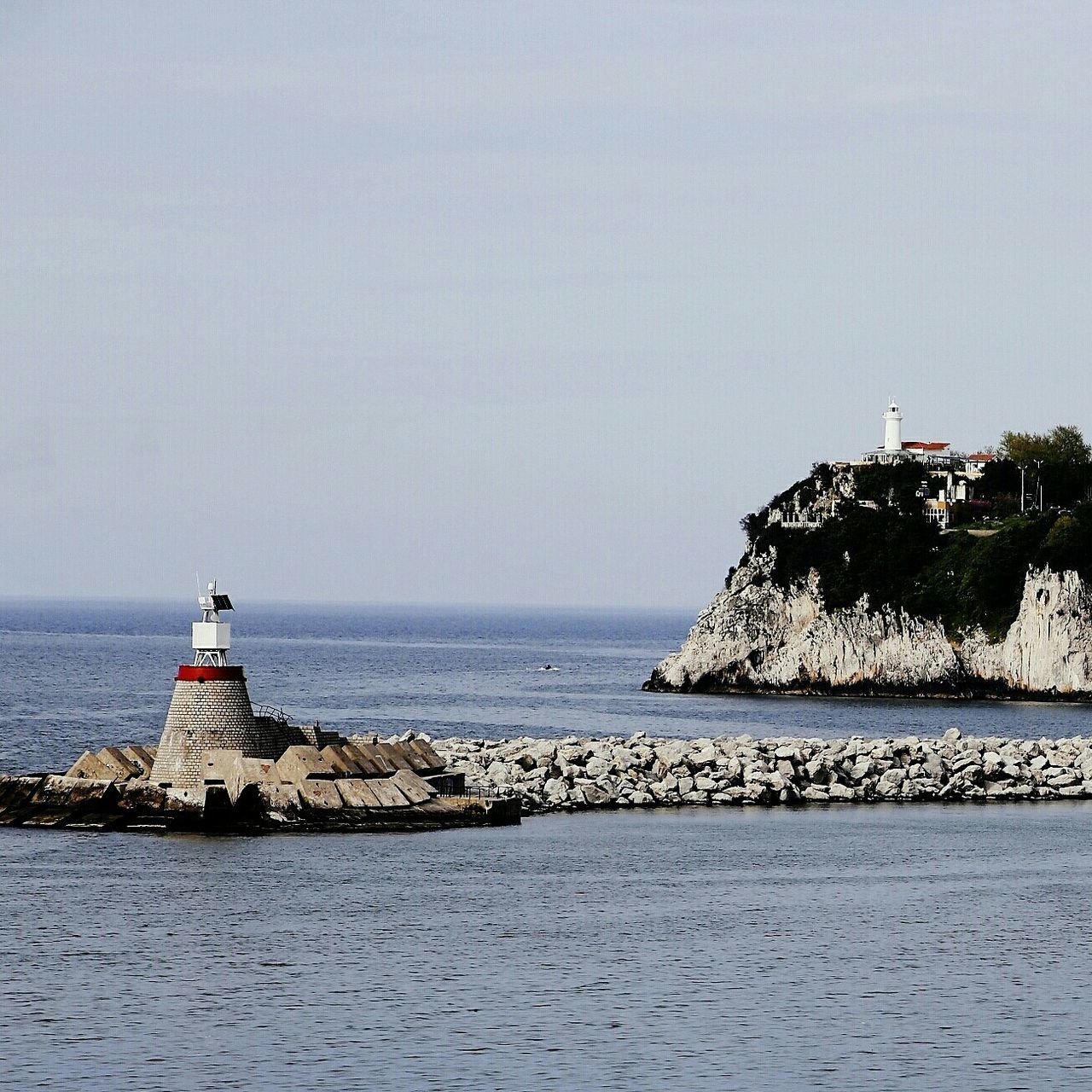 sea, water, clear sky, horizon over water, copy space, lighthouse, waterfront, built structure, tranquil scene, architecture, scenics, building exterior, tranquility, guidance, beauty in nature, nature, beach, protection, direction, shore