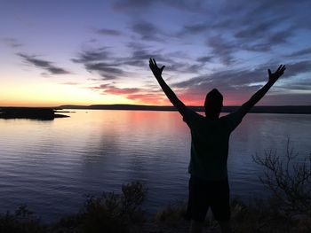 Rear view of silhouette person standing by lake against sky during sunset