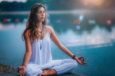 Woman doing yoga while sitting on pier at lake