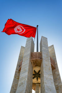 Low angle view of flag against building against clear blue sky