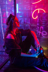 Caucasian woman in neon studio behind chain-link mesh. 