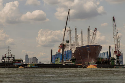 Cranes at harbor against cloudy sky