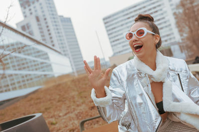 Smiling woman in sunglasses gesturing against building