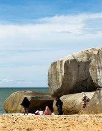 People sitting on beach by sea against sky