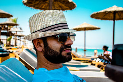 Close-up of man wearing sunglasses relaxing at beach against sky