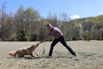 Adult man playing with his dog in a field on the hills in springtime