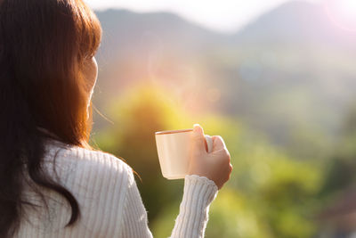 Rear view of woman holding coffee cup outdoors