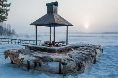 Lifeguard hut on frozen sea against sky during sunset