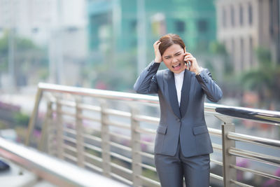 Angry businesswoman talking on mobile phone on bridge in city