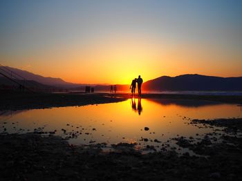 Silhouette people on beach against sky during sunset