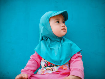 Cute baby boy looking away against blue wall