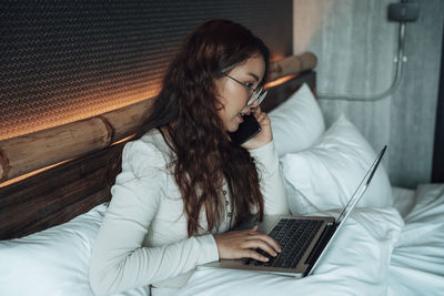 Young woman using mobile phone while sitting on bed