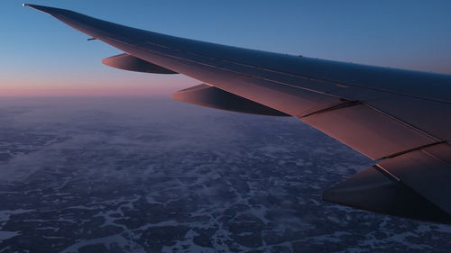 Cropped image of aircraft wing flying against sky during sunset