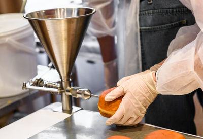 Midsection of man using appliance while filling donut at factory