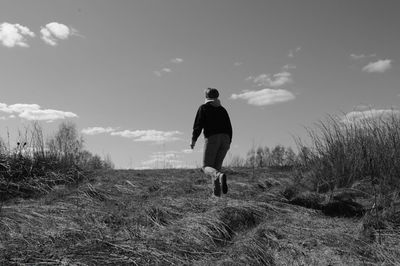 Rear view of man standing on field against sky