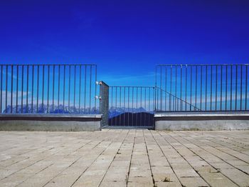 Railing by sea against clear blue sky